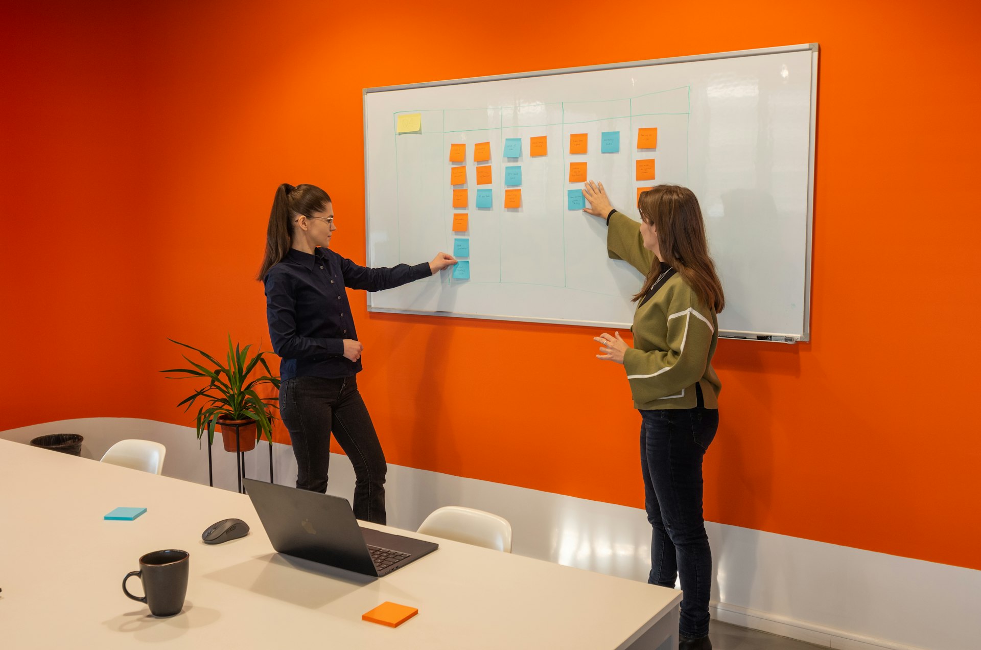 two women standing in front of a white board